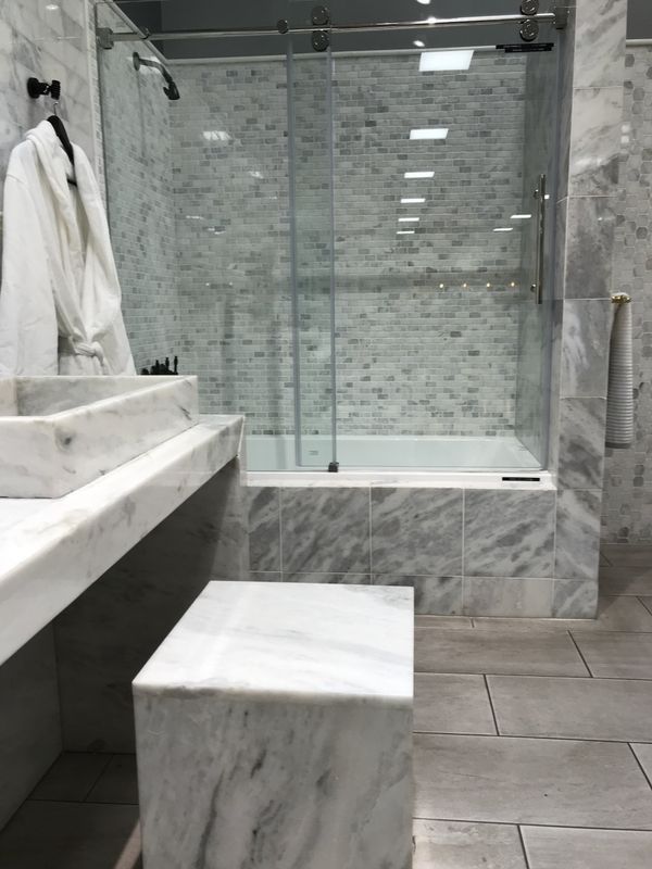 Bathroom with marble tiling, glass shower, bathtub, and marble bench. White robe hanging nearby.