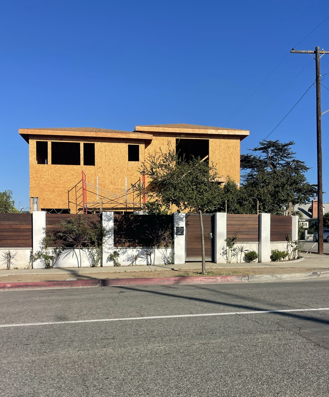 Construction worker on roof frame, carrying wood plank; house under construction.