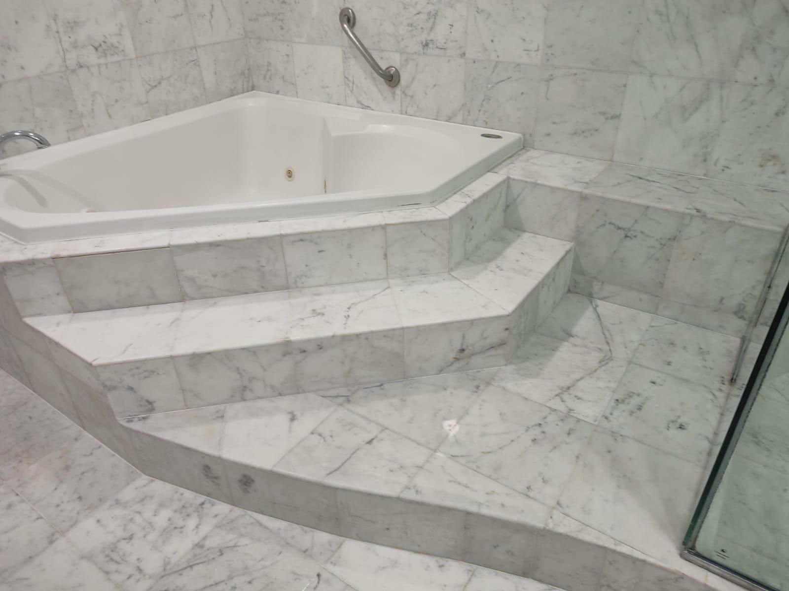 White marble bathroom with a built-in, triangular bathtub, accessed by marble steps.