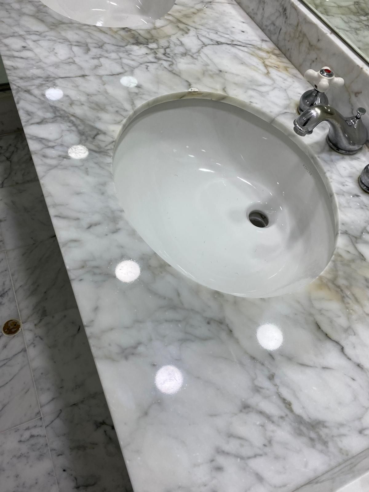 White oval sink on a marble countertop with silver faucet.