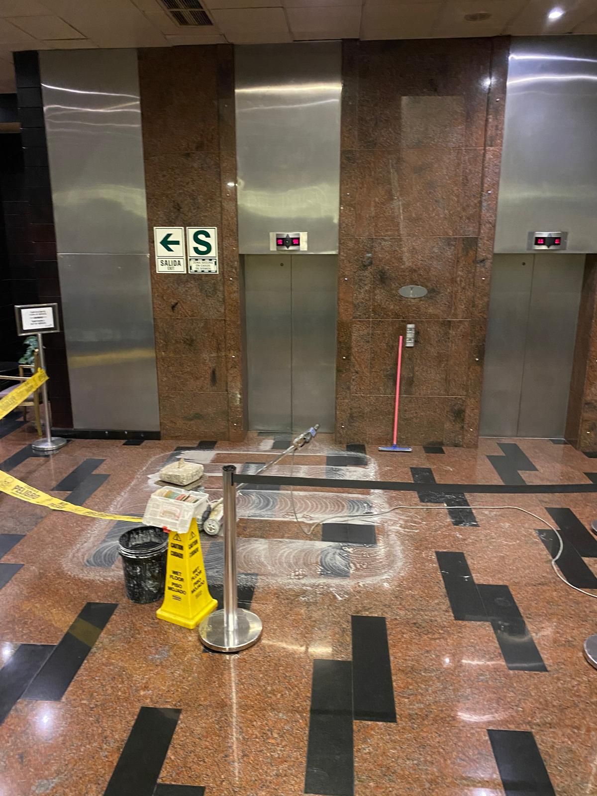 Elevator lobby: damaged floor, caution tape, closed elevator doors. 