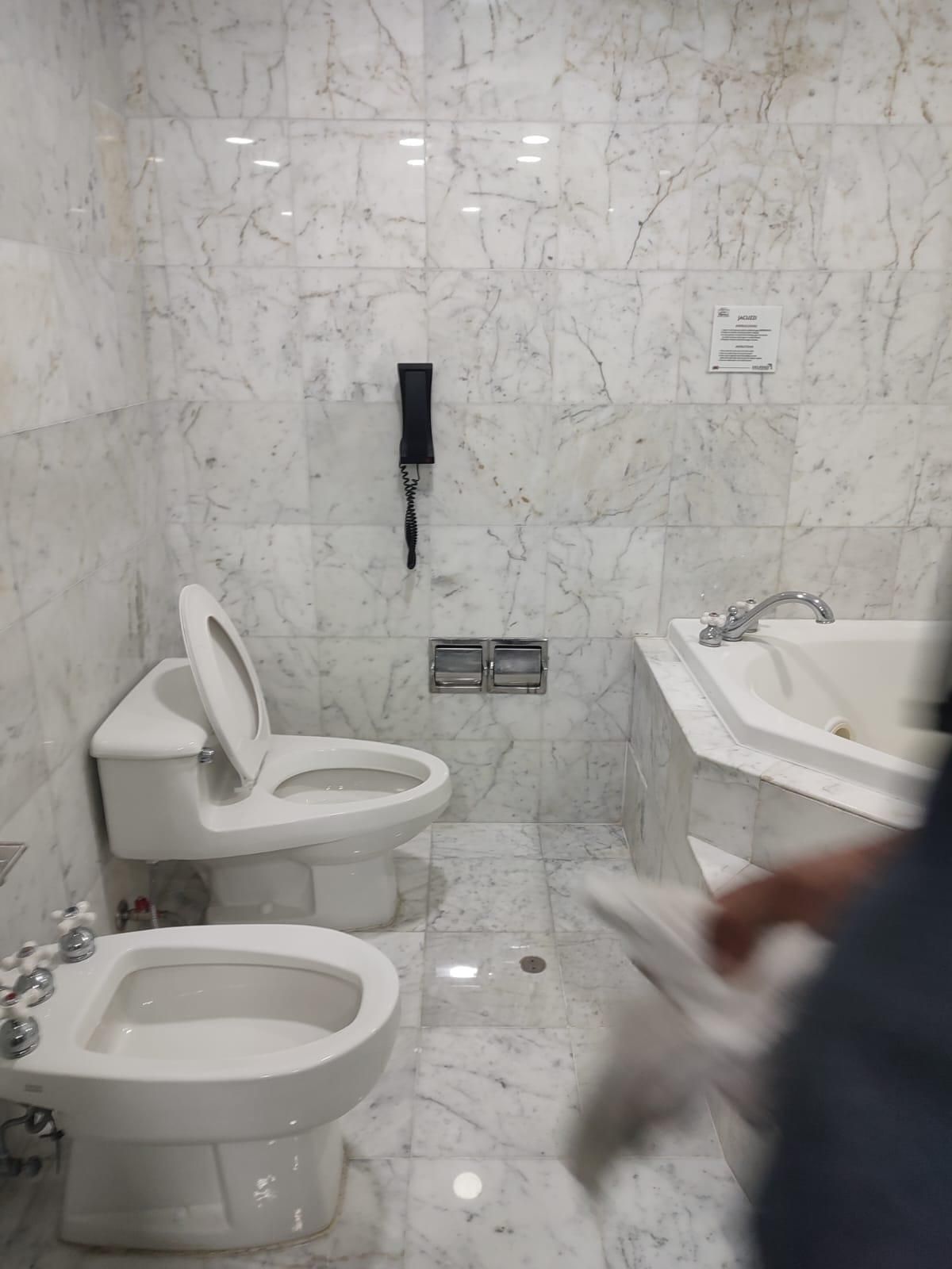 Marble bathroom with toilet, bidet, and jacuzzi. A person is reaching towards the jacuzzi.