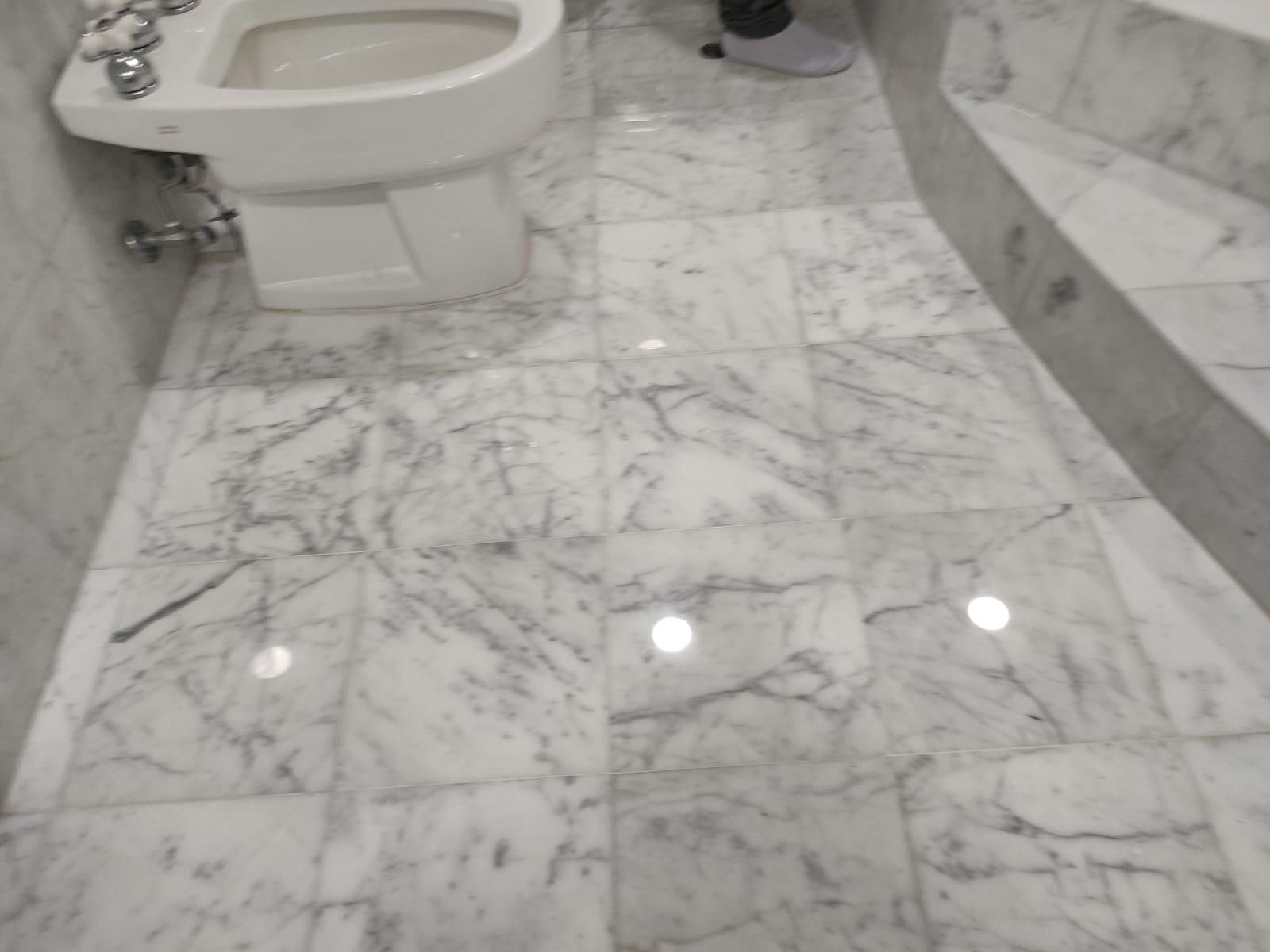 White marble bathroom floor and bidet, person's legs visible, bright lighting, reflective surface.