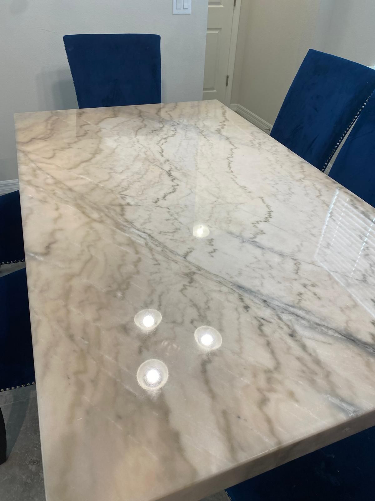 Marble dining table with four blue velvet chairs in a well-lit room.