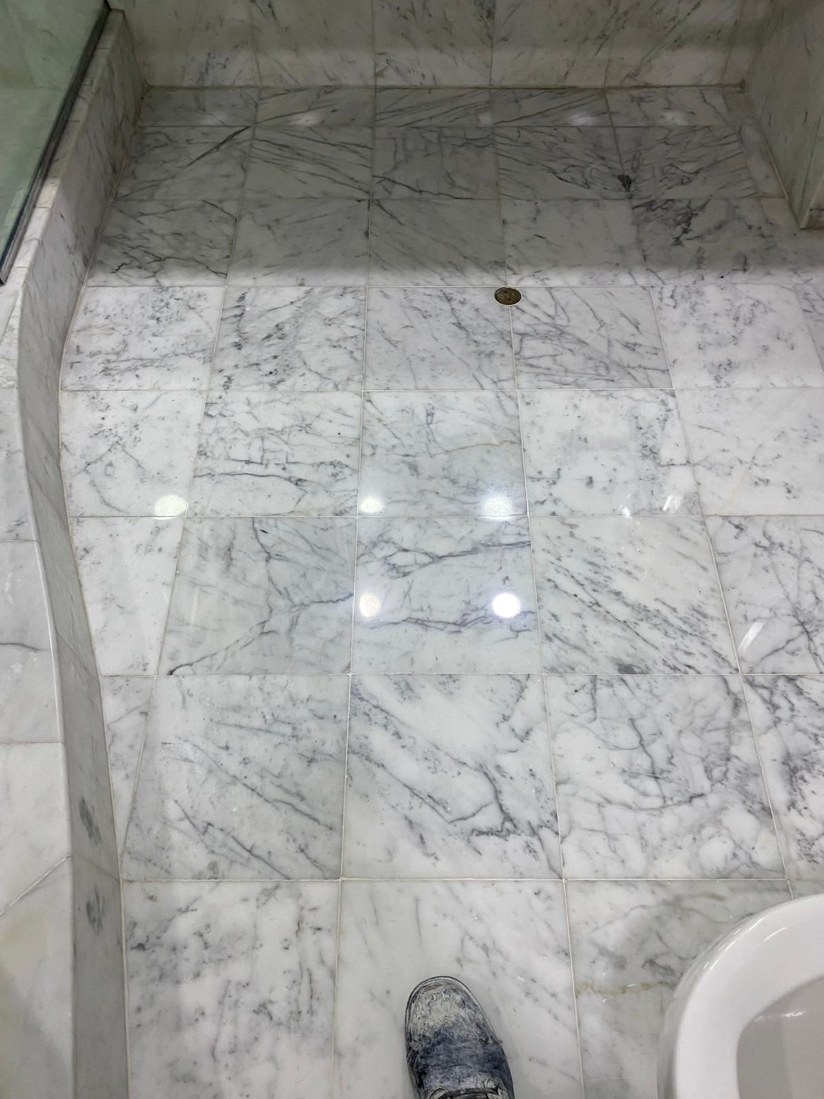 White marble tiled bathroom floor with dark veining and a shoe in the foreground.