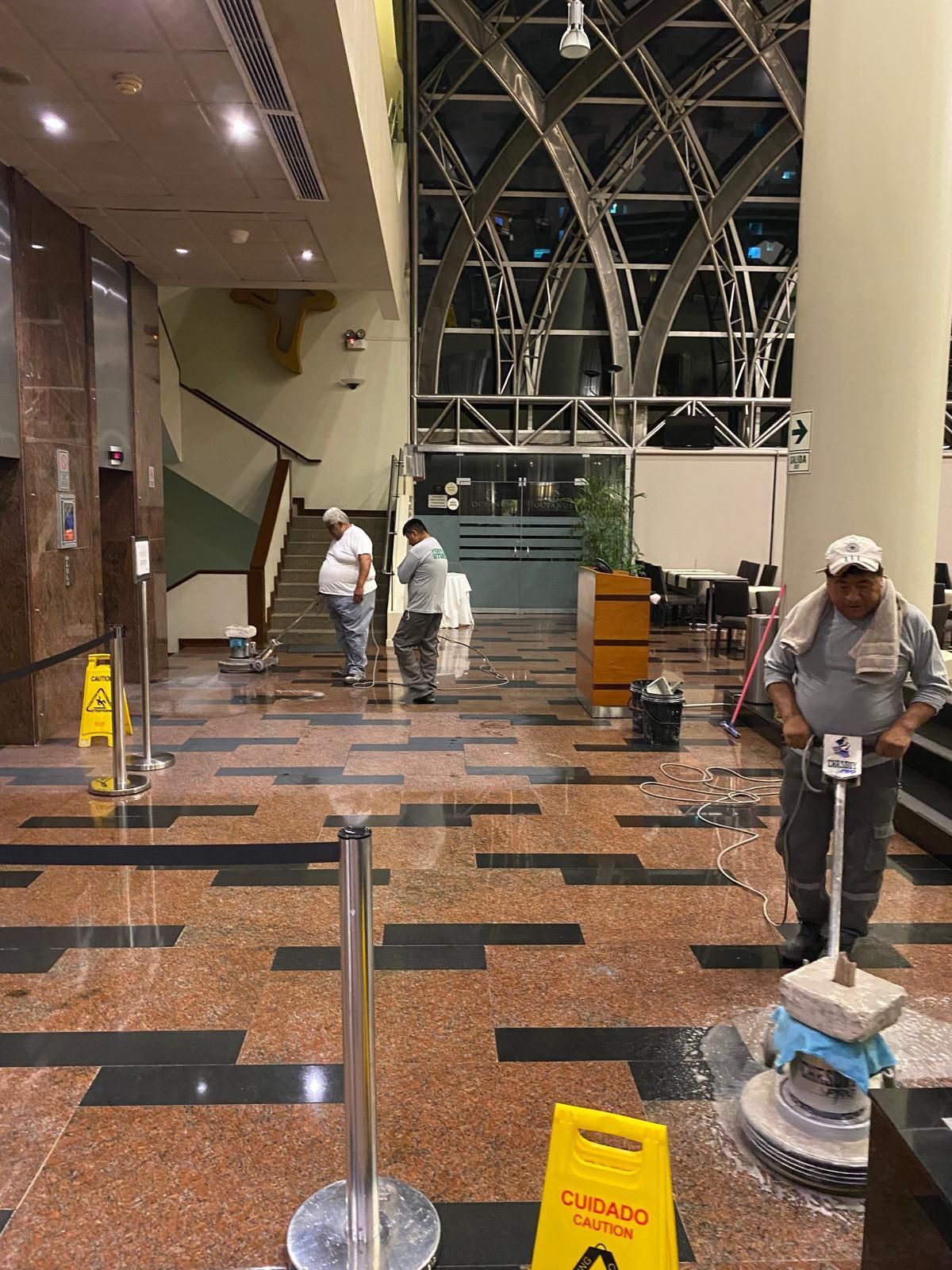 Workers polishing a lobby floor, using machines, and setting up caution signs.
