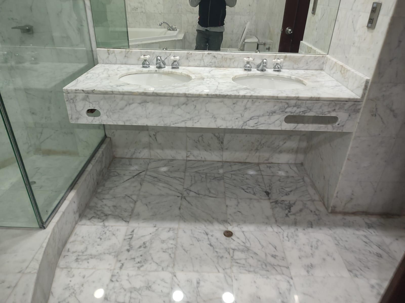 Marble bathroom with double sinks and glass shower. Floor and counter are marble.