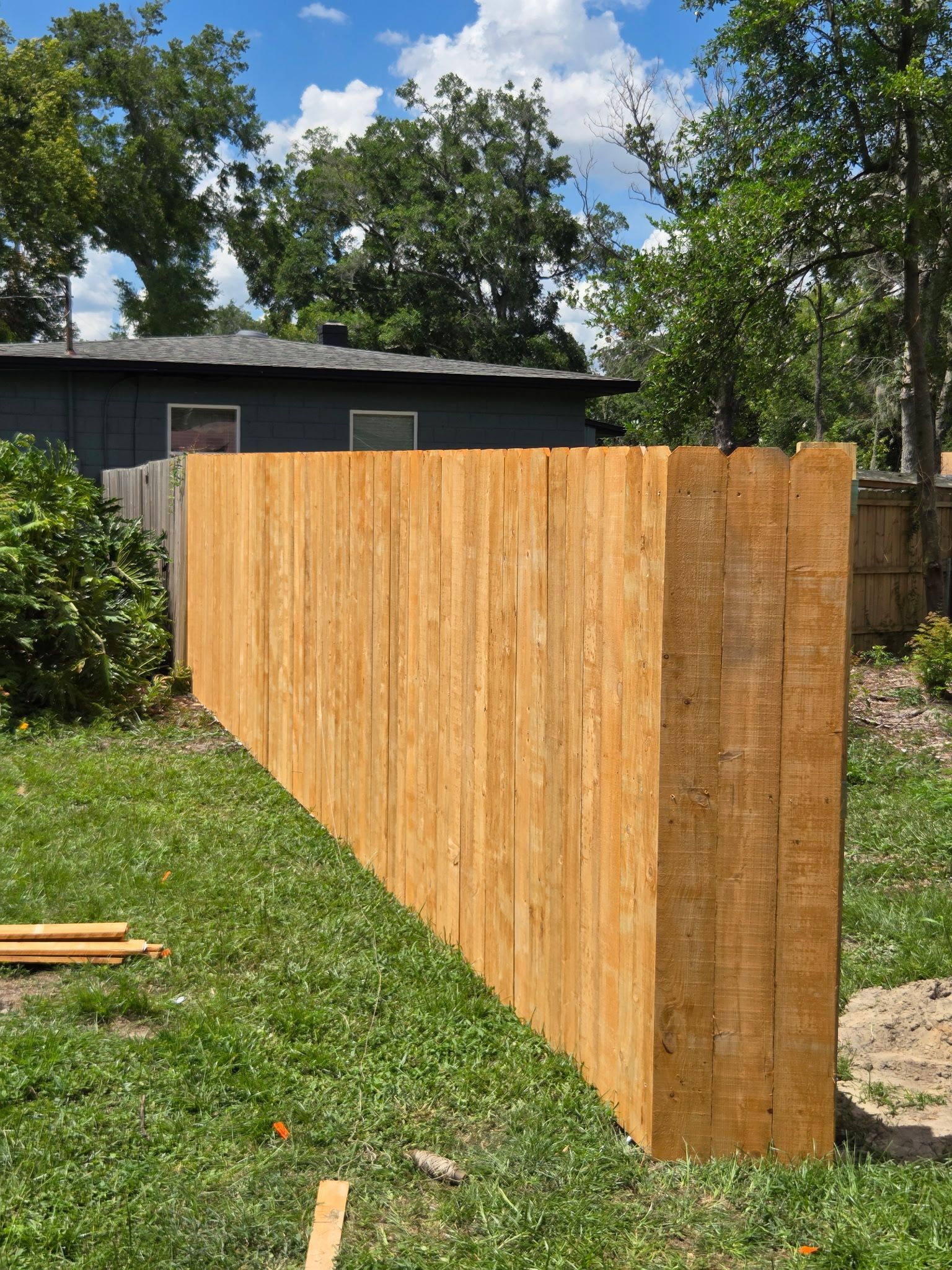 Wooden privacy fence with lattice top in a wooded setting.