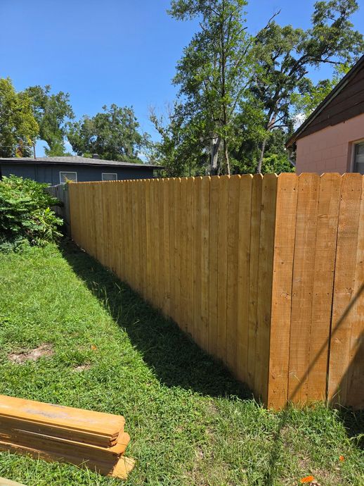 Modern fence with black metal and brown wood slats, next to a brick and concrete walkway.