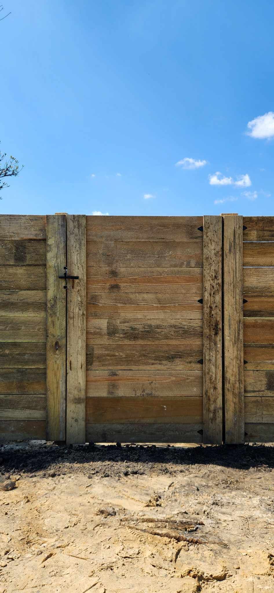 Gray privacy fence on a white retaining wall, with greenery in front and behind.