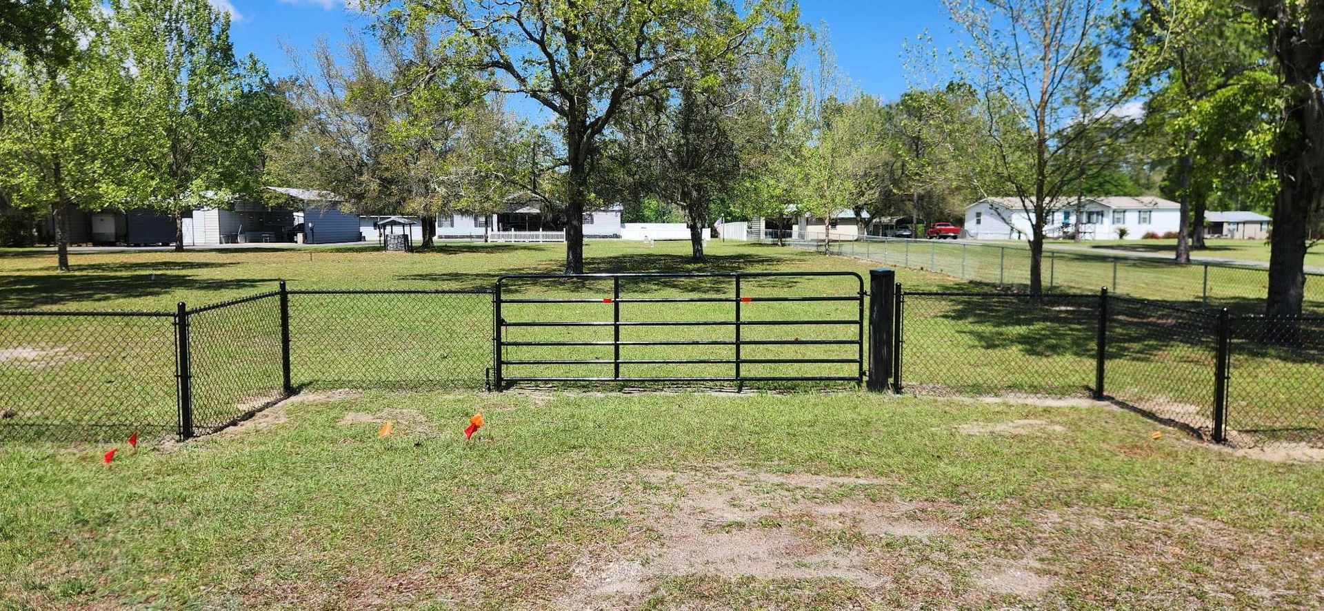 Brown wooden fence along a road with green grass and trees under a blue sky.