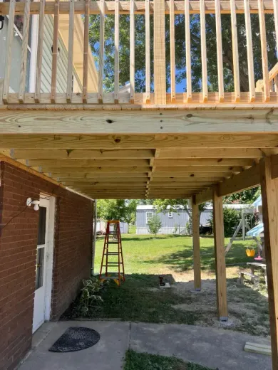 Two-story wooden deck with a covered lower level; next to a brick building and yard.