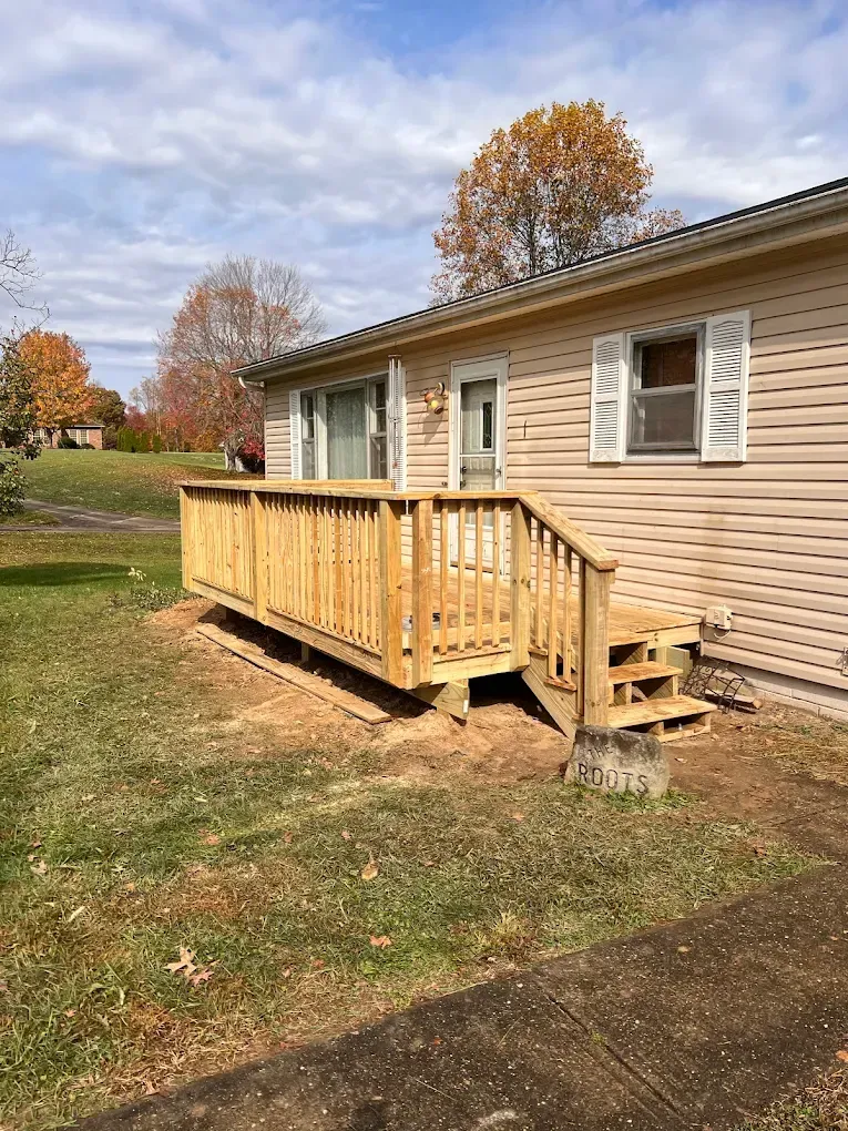 A wooden deck with railing and steps attached to a tan house with white shutters on a lawn.