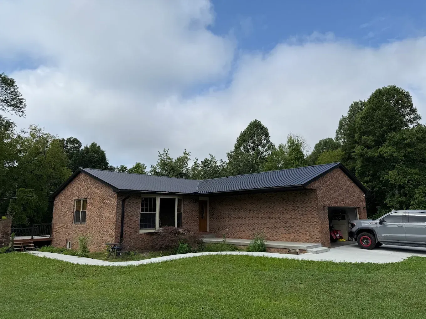 Brick house with dark roof and a car parked in the driveway under a cloudy sky.