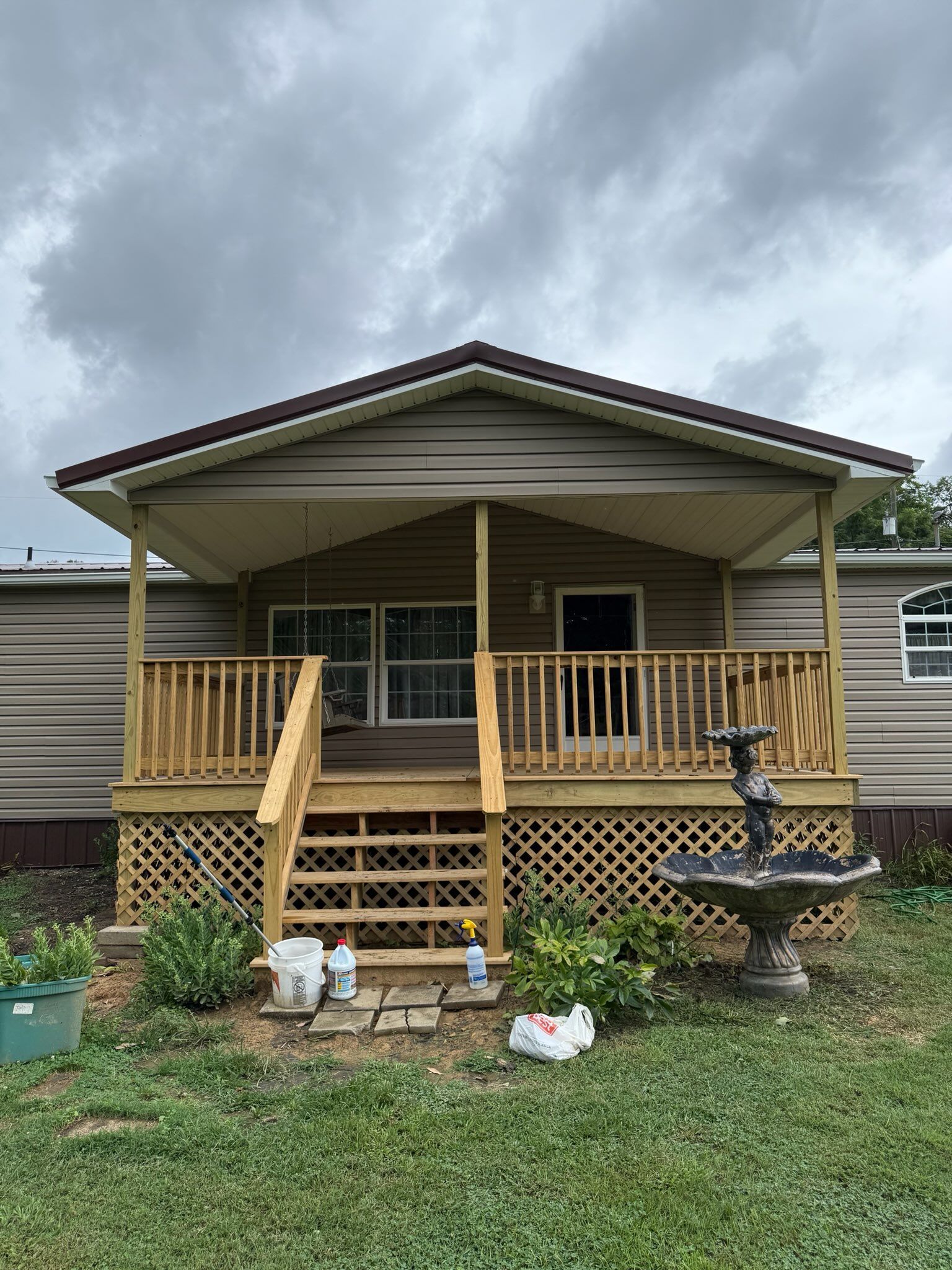 White house with chimney, porch, and overgrown yard on a cloudy day.