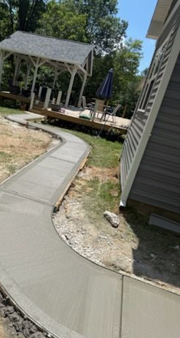 Newly poured concrete sidewalk curving toward a deck with a gazebo; sunny day.