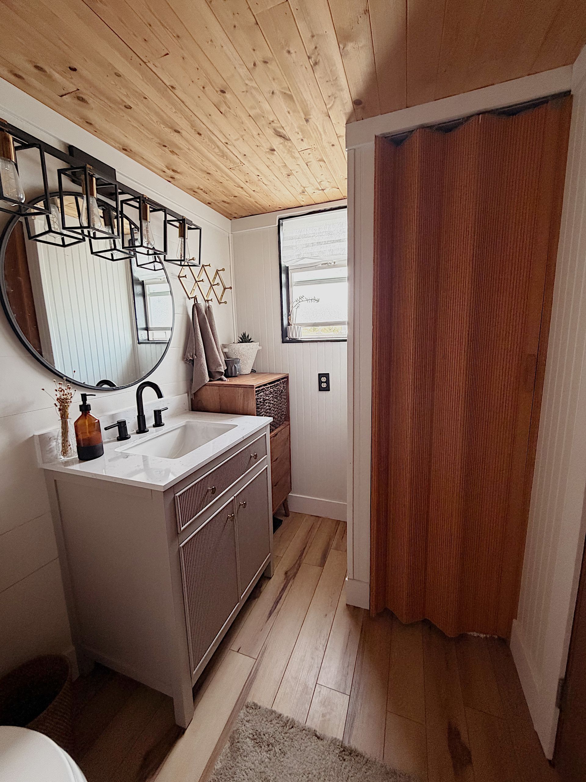 Interior of a tiny house with wood floors and ladder to a loft. Door opens to outdoor greenery.