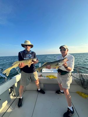 Two men are standing on a boat holding large fish.