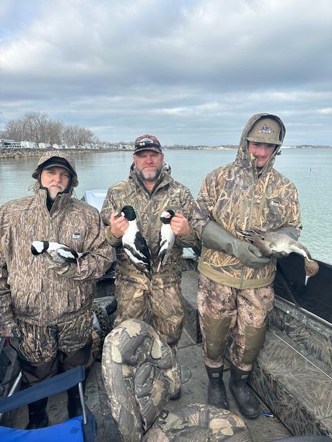 Three men are standing on a boat holding ducks.