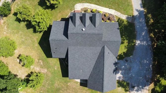 an aerial view of a house with a black roof surrounded by trees and grass .