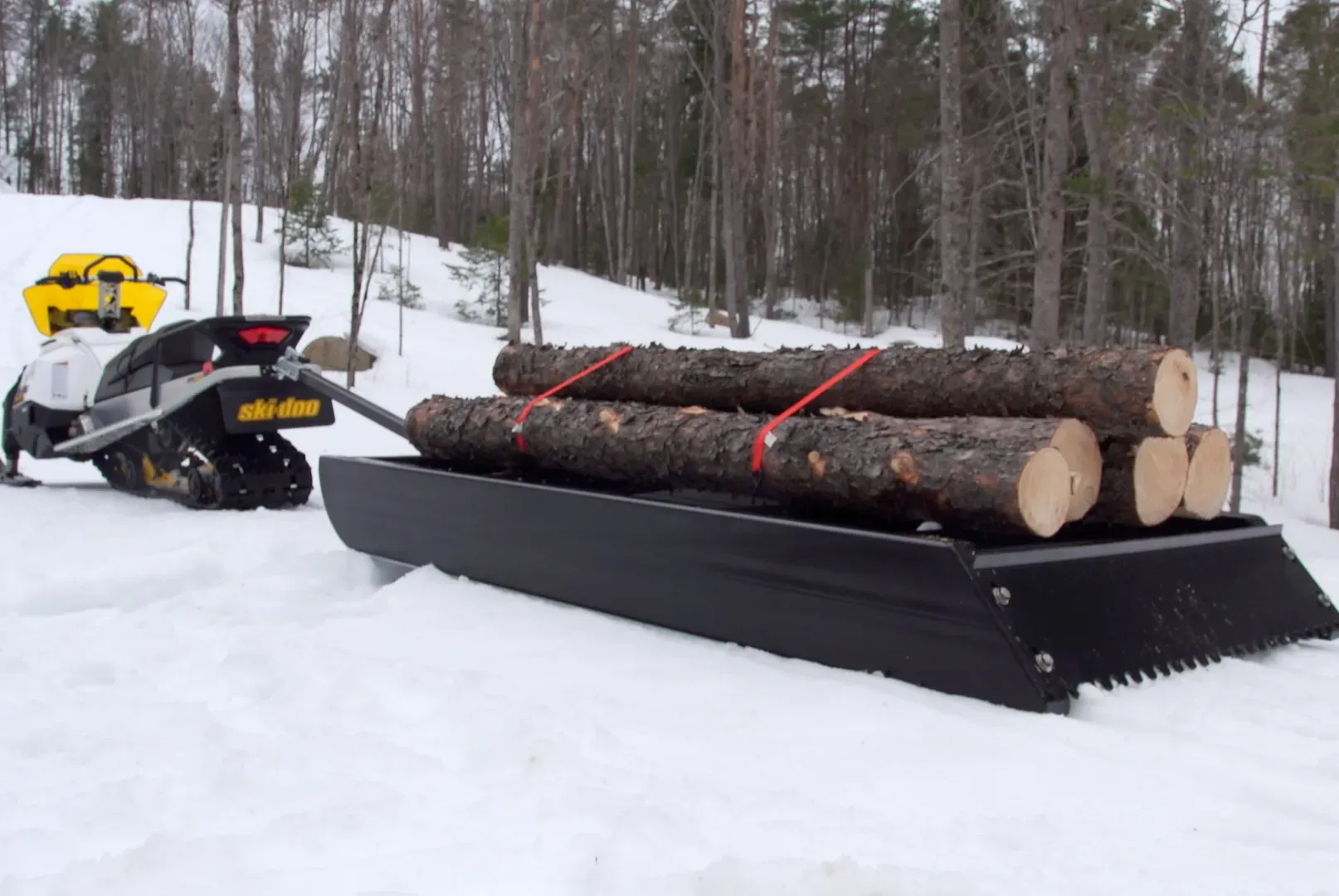 A snowmobile pulling a sled full of logs in the snow