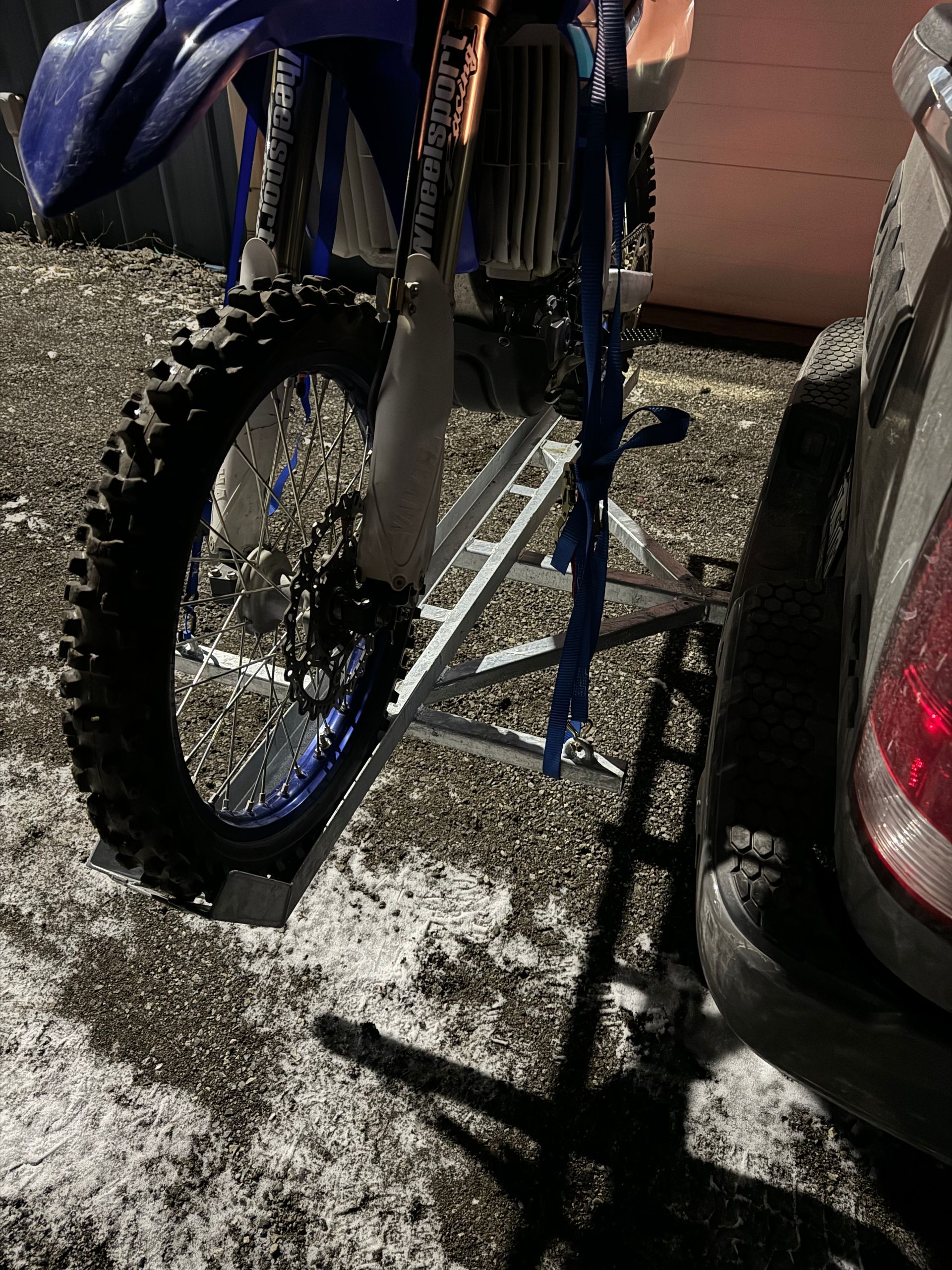 A dirt bike is parked next to a car in the snow.