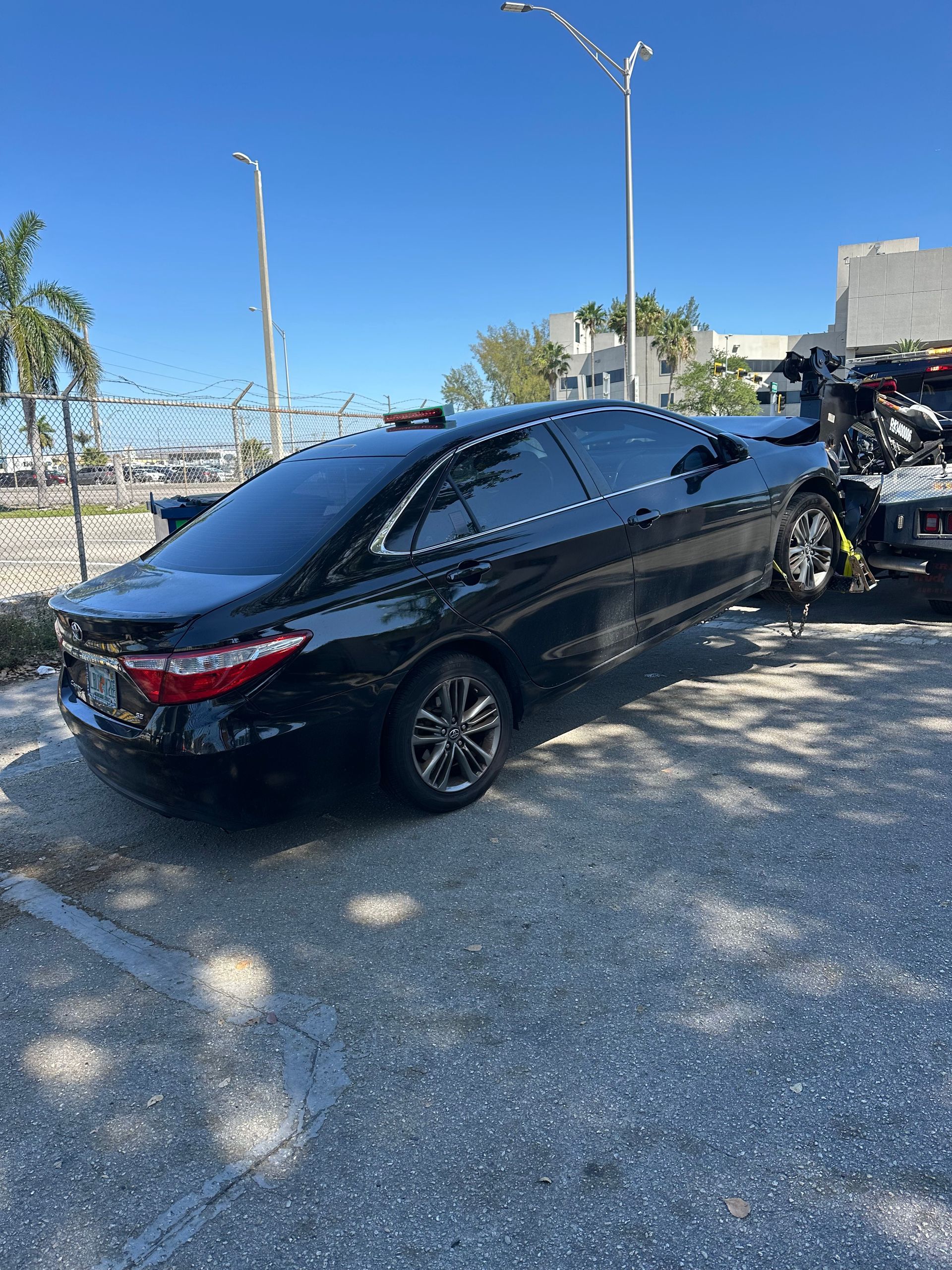 Car towing service in Miami-Dade – black Toyota Camry being towed with wheel-lift tow truck for roadside assistance.