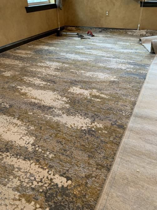 Worker using a cutter to carefully install new carpet flooring in a room, ensuring precise measurements and smooth placement.