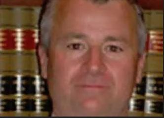 Headshot of a person with short hair against a background of stacked law books with red and black spines.