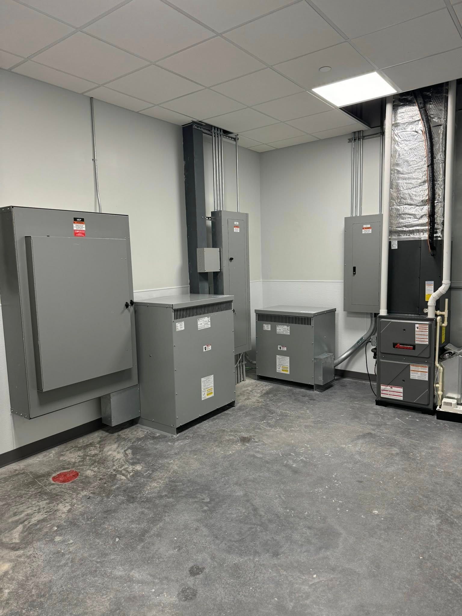 An interior view of a utility or mechanical room featuring several grey electrical cabinets, power units, and a furnace.