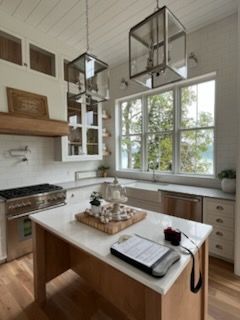 A bright, modern kitchen features a wooden island with a clipboard, white cabinets, and large hanging pendant lights.