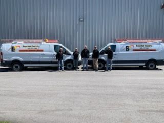 Five people stand between two white utility vans branded with 