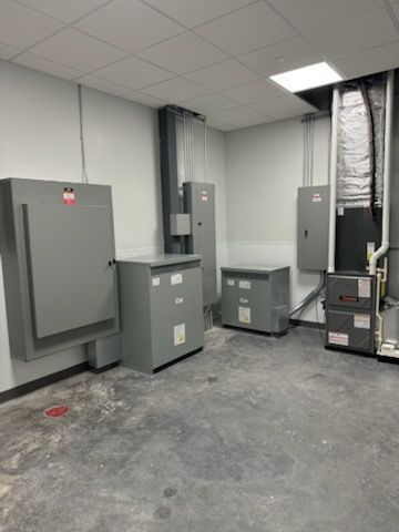 Electrical room with gray metal cabinets, transformers, and HVAC equipment installed against light gray walls.