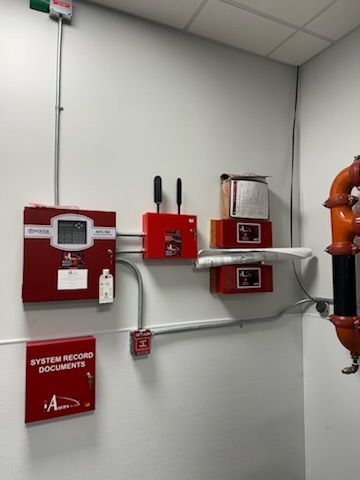 Fire alarm control panel, communication equipment, and a system document cabinet mounted on a wall in a mechanical room.