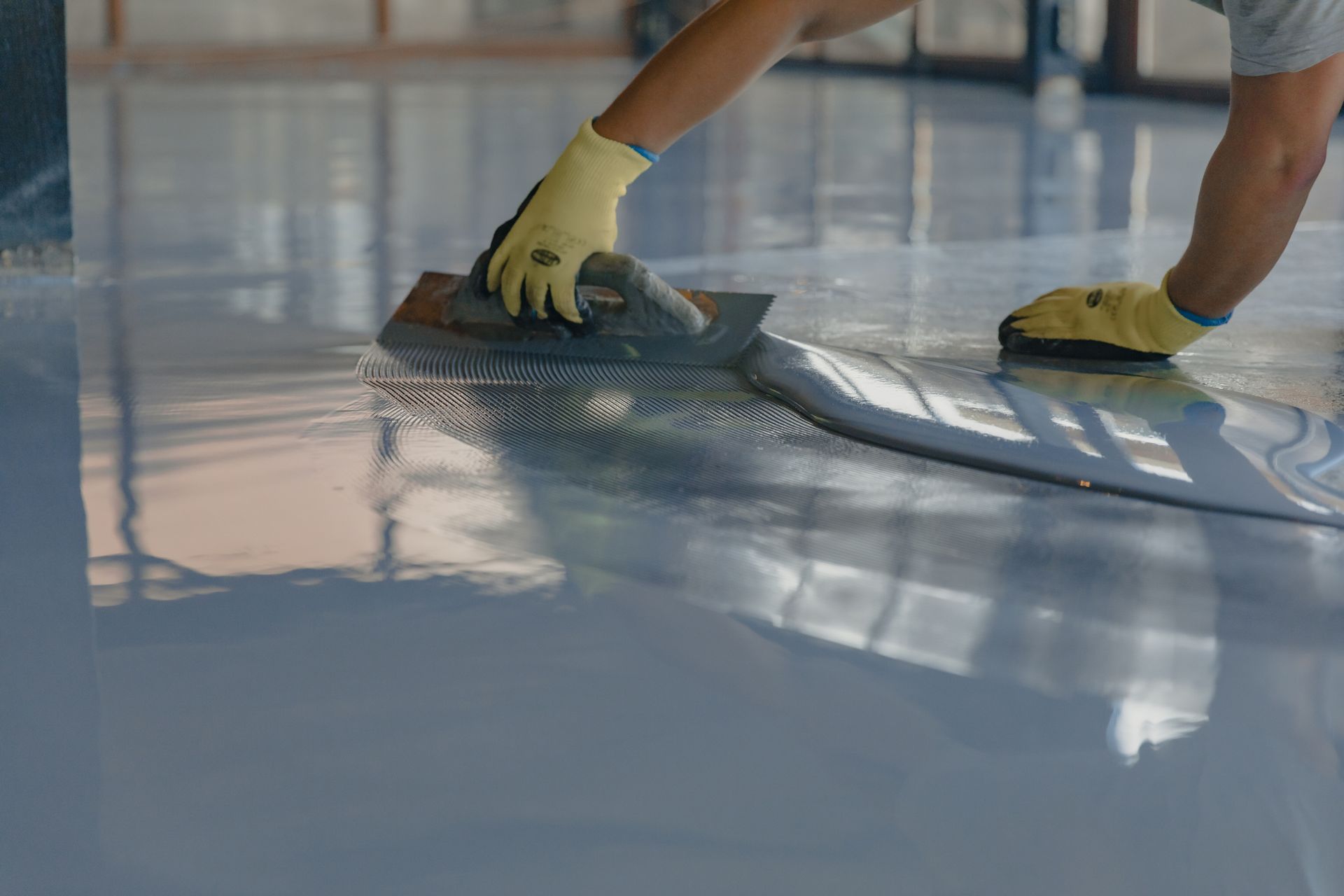 A person is applying a coating to a concrete floor with a trowel.