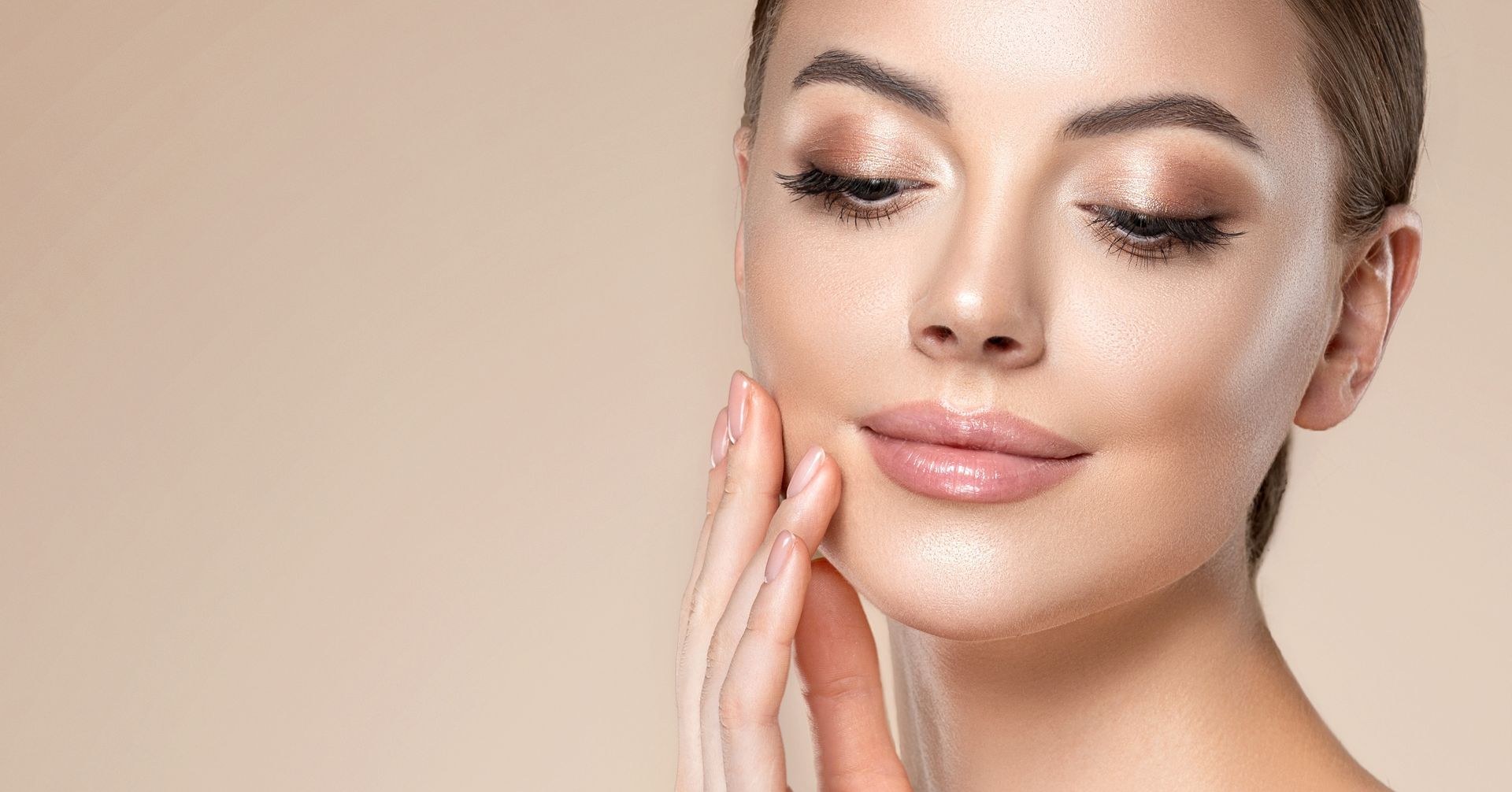 Woman with fair skin, wearing makeup, touching her cheek gently, with a neutral background.