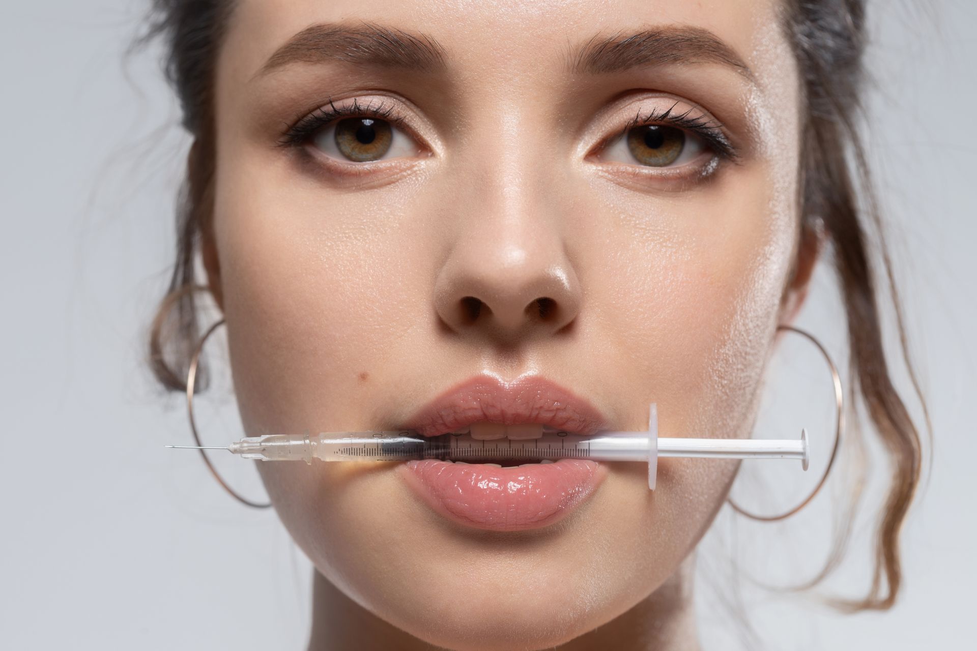 Woman with a syringe in her mouth; she has full lips, hoop earrings, and a neutral expression.