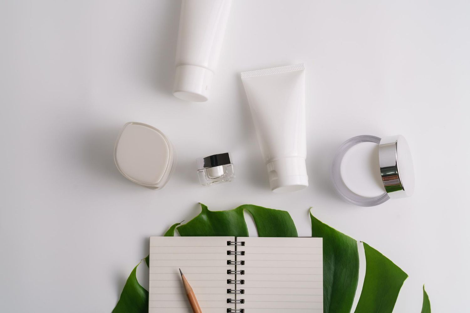A notebook , a pencil , a leaf , and tubes of cosmetics on a table.