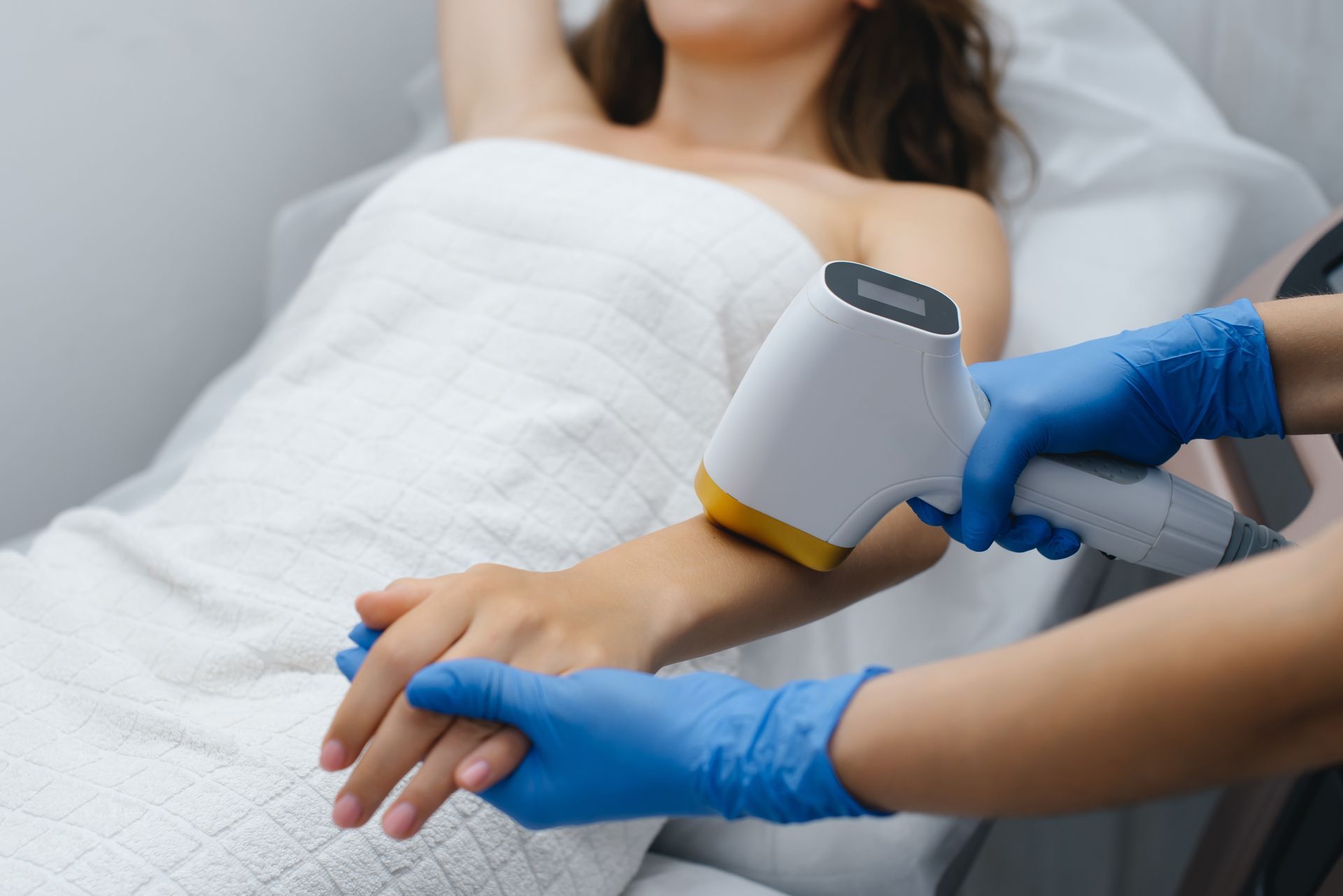 Woman receiving laser hair removal on arm by gloved hands.