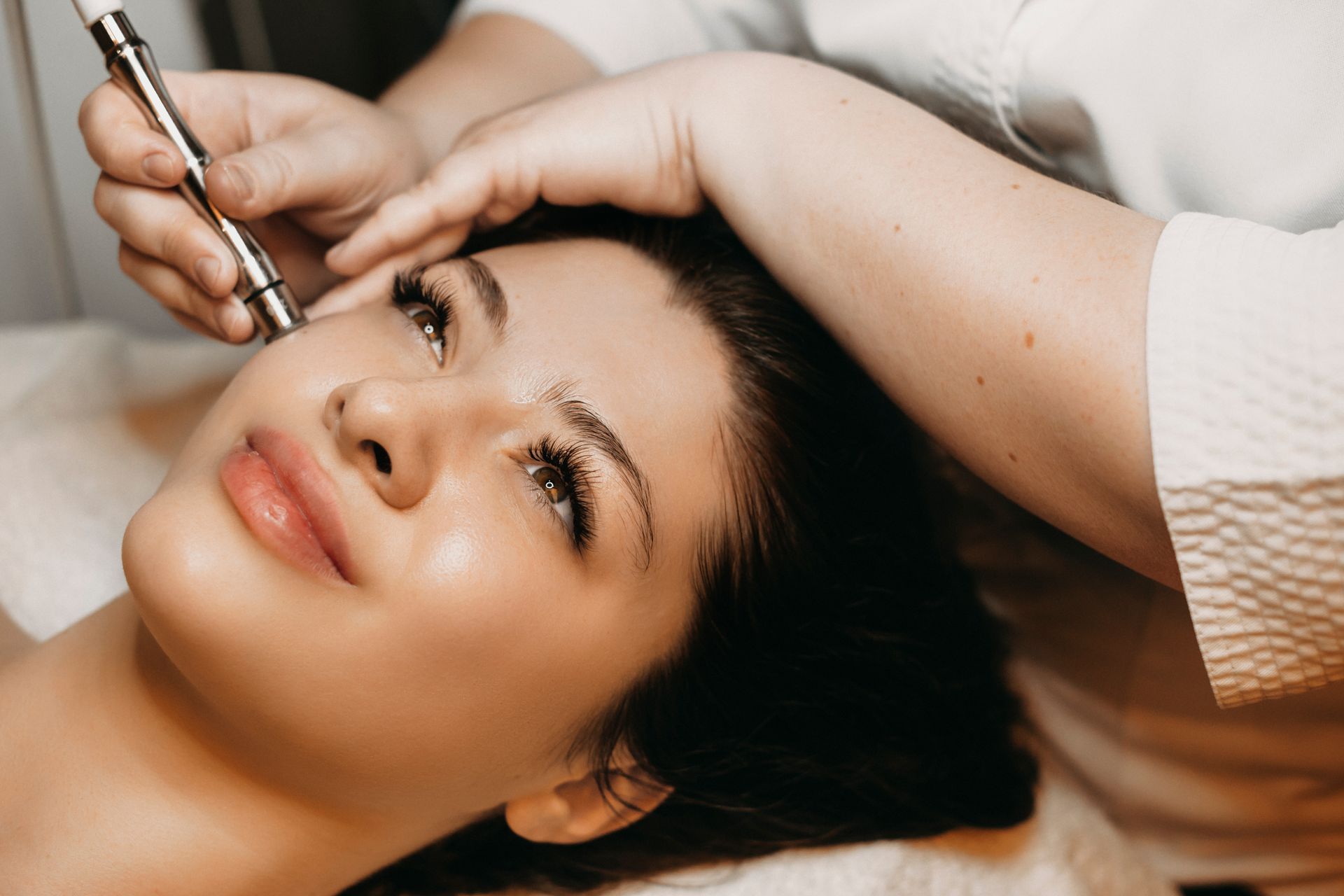 Person receiving a facial treatment with a handheld device while lying on a spa bed