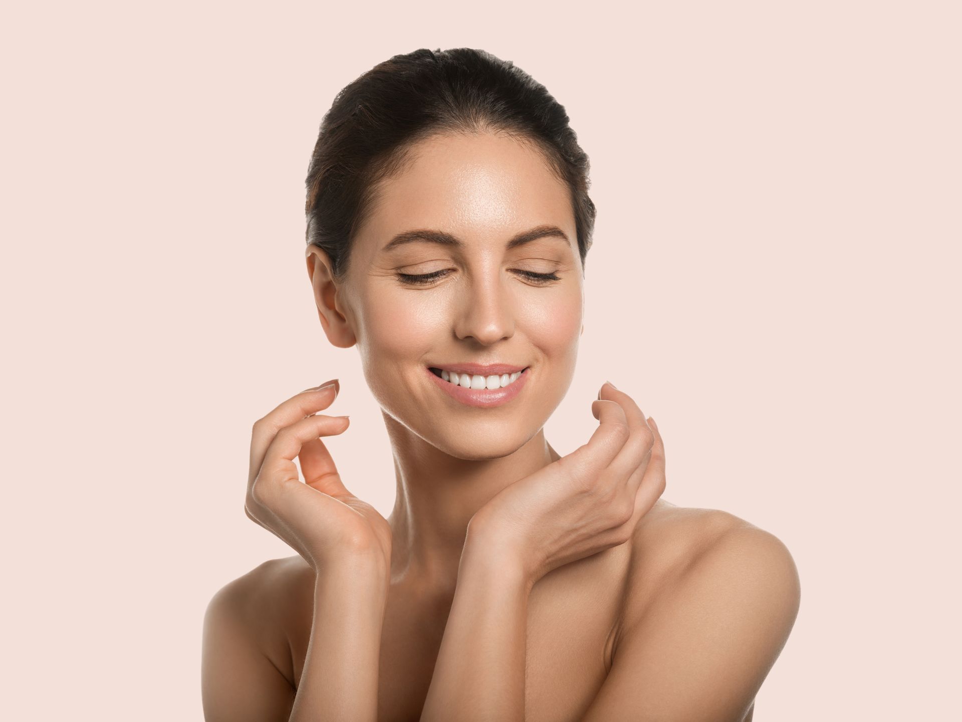 A woman is smiling with her eyes closed and touching her face.