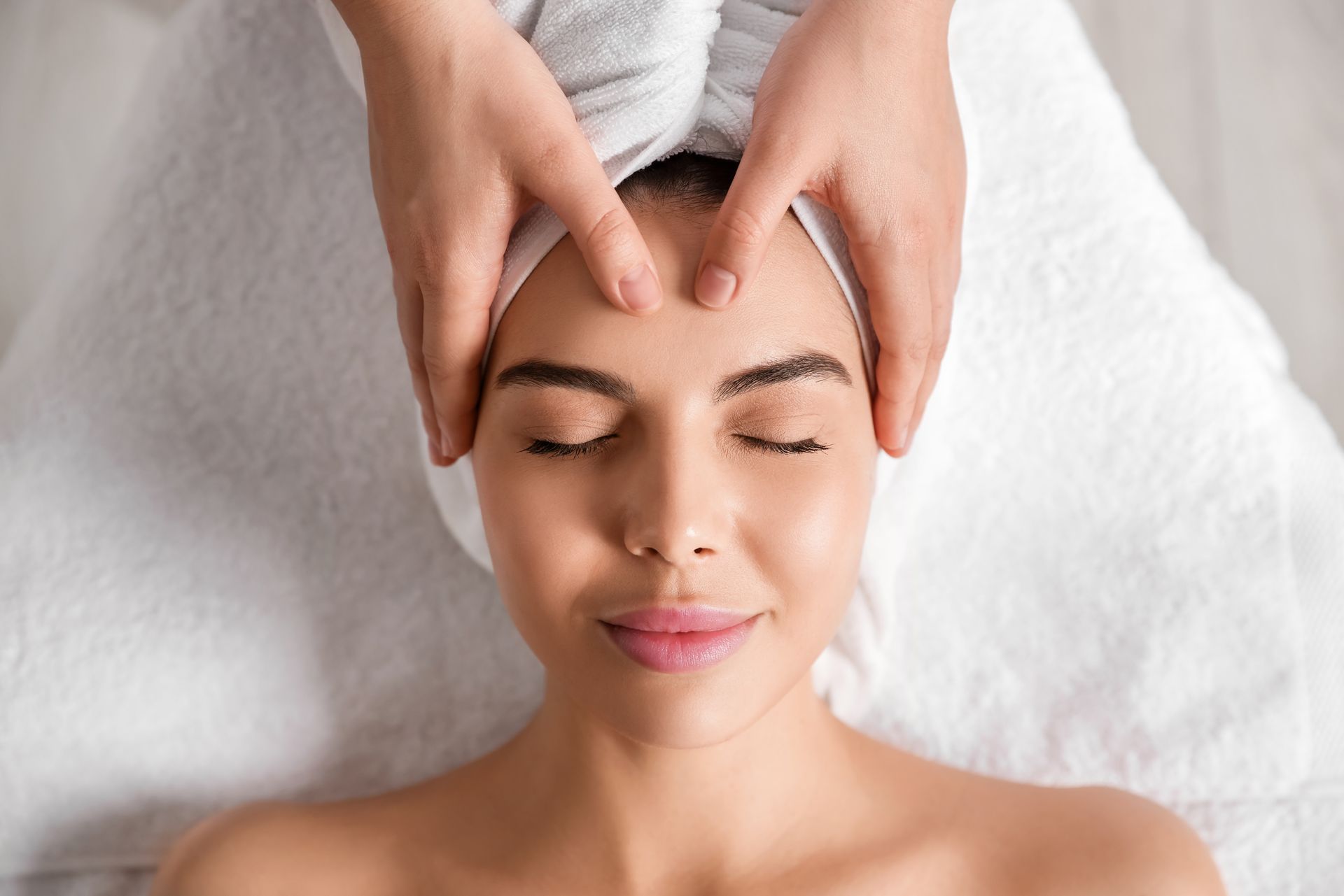 A woman with a towel wrapped around her head is getting a head massage at a spa.