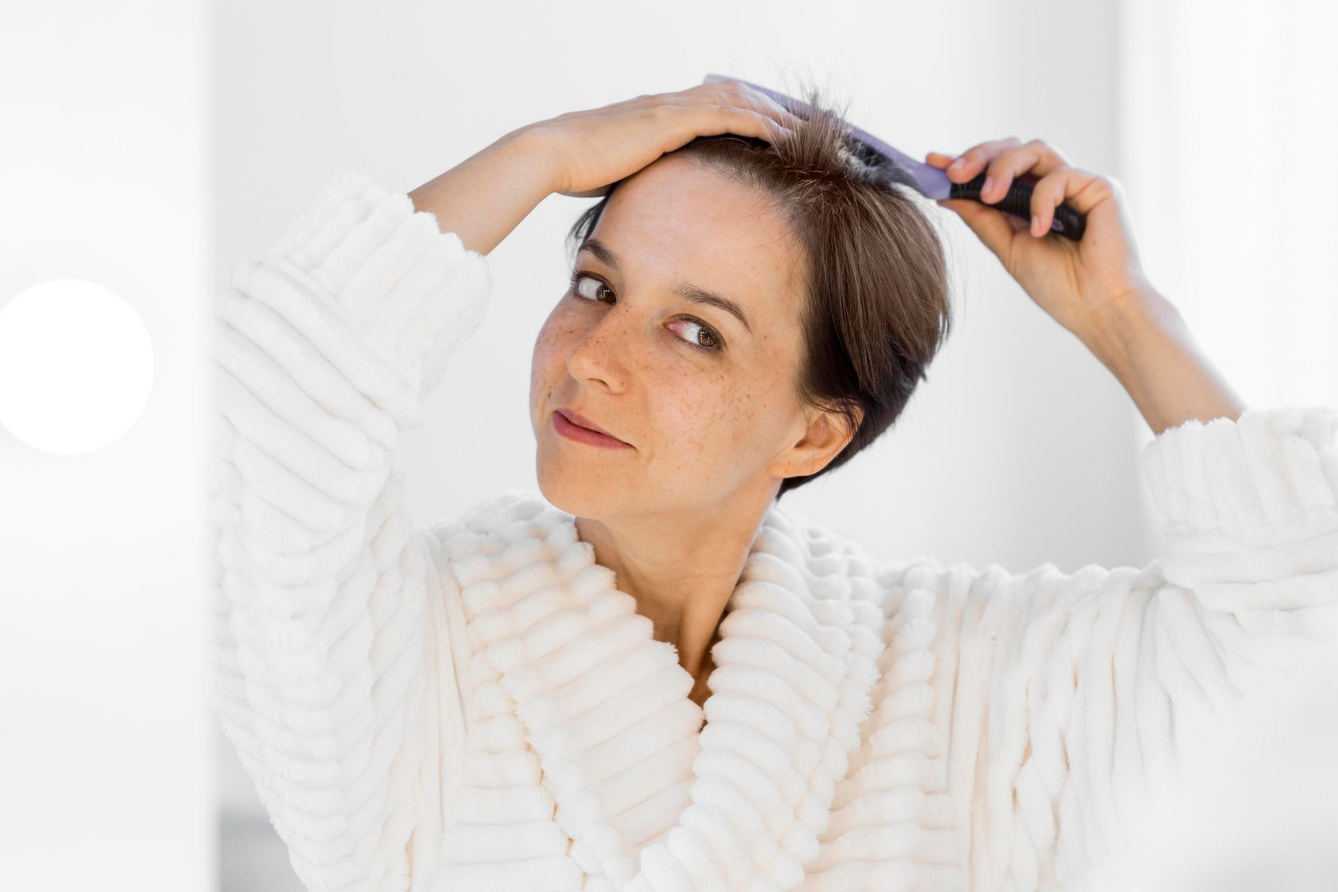 A woman in a white robe is brushing her hair.