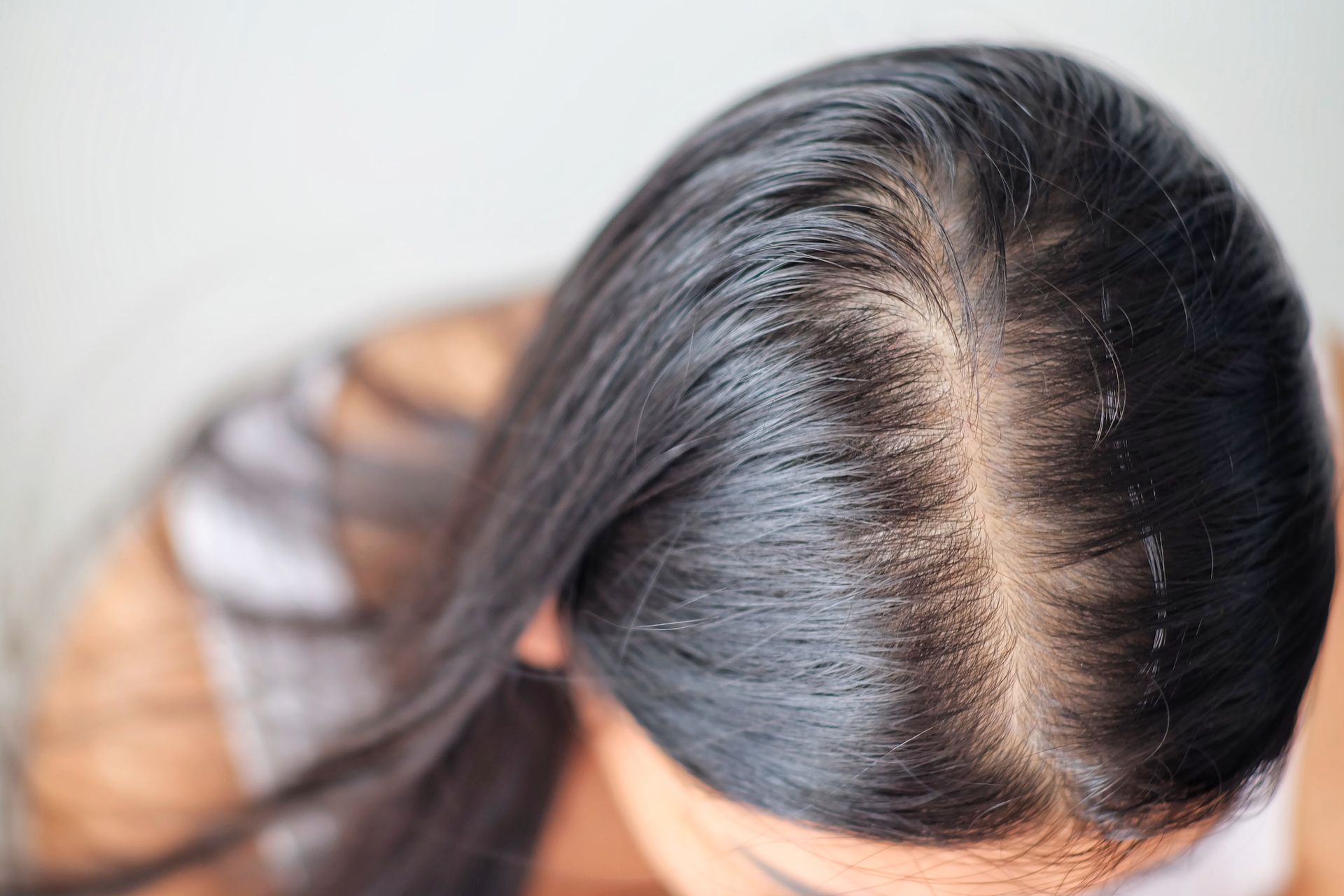 A woman with long black hair is looking down at her hair.