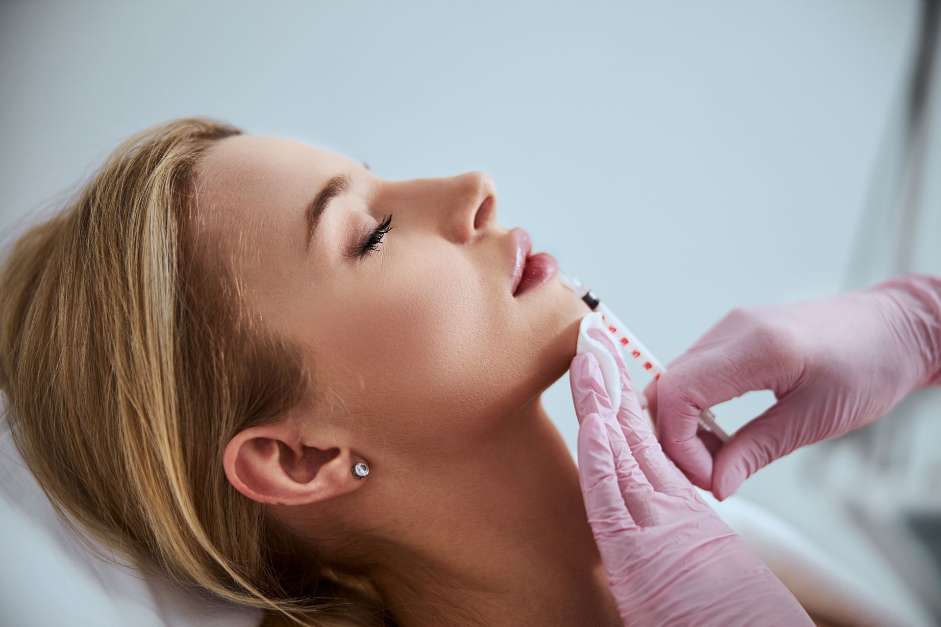 Person receiving lip injections. A gloved hand uses a syringe near the subject's mouth.