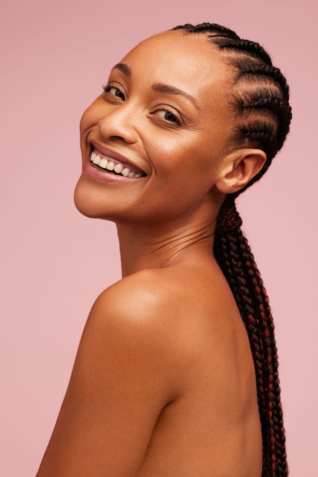 A woman with braids is smiling and looking over her shoulder.