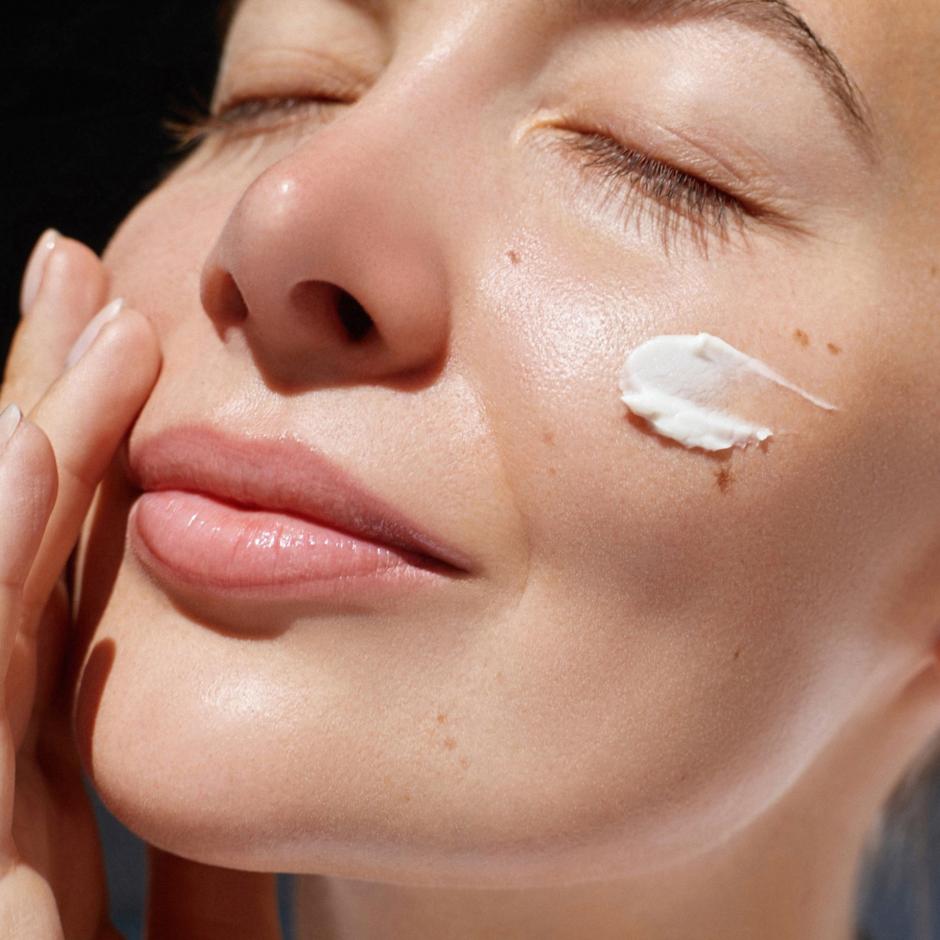 A close up of a woman applying lotion to her face