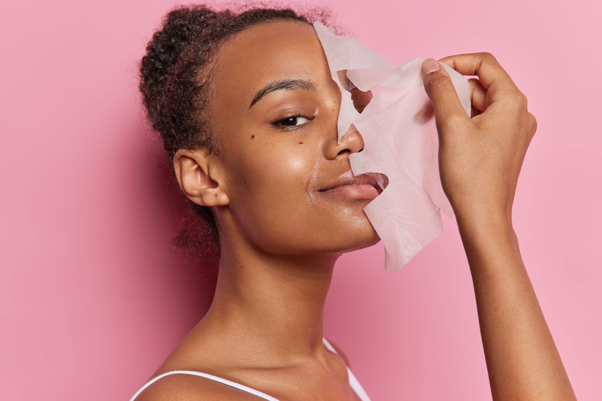 A woman is applying a sheet mask to her face.