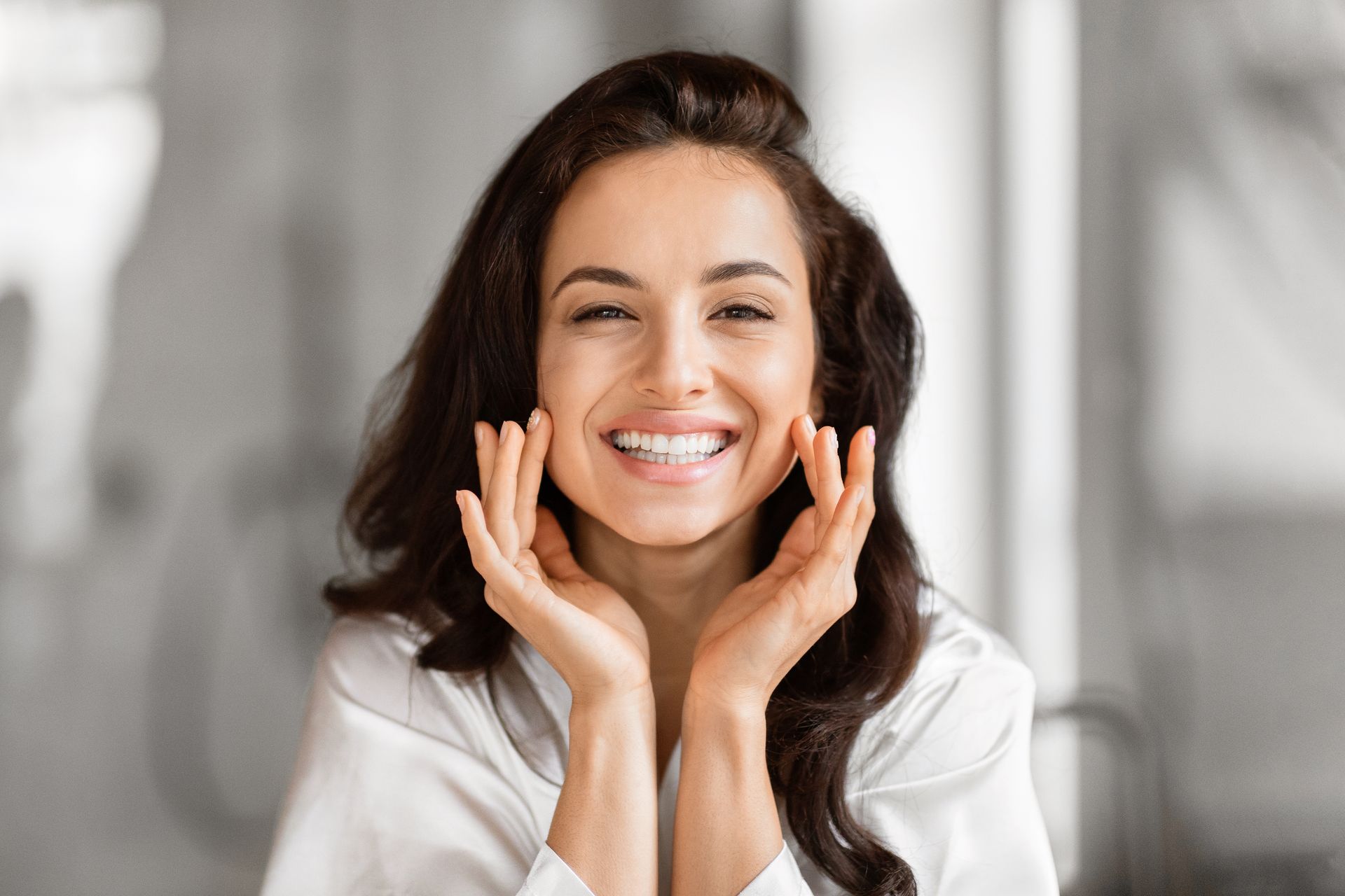 A woman is smiling with her hands on her face.