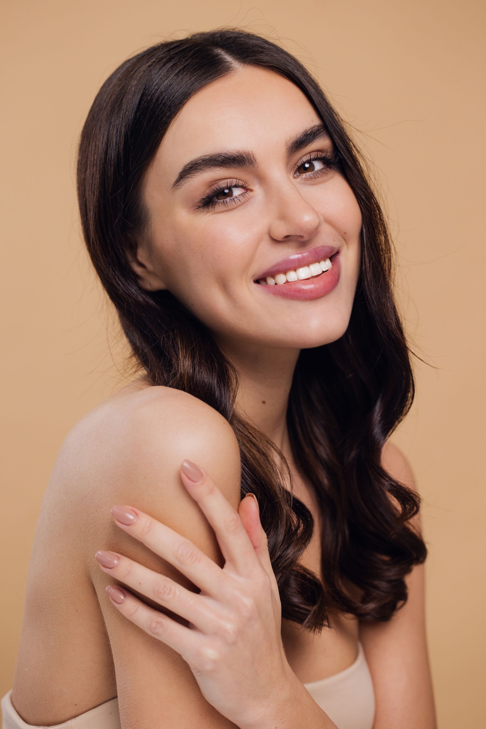 A woman with long hair is smiling and holding her shoulder.